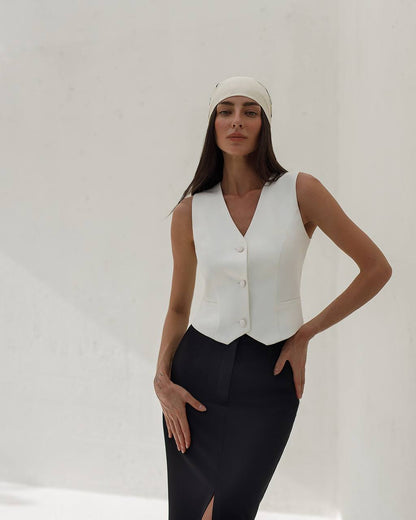 Woman wearing a white sleeveless top and black pants against a plain background