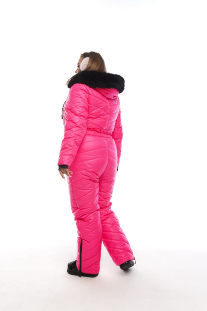 Person wearing a bright pink snowsuit with black fur trim on a white background