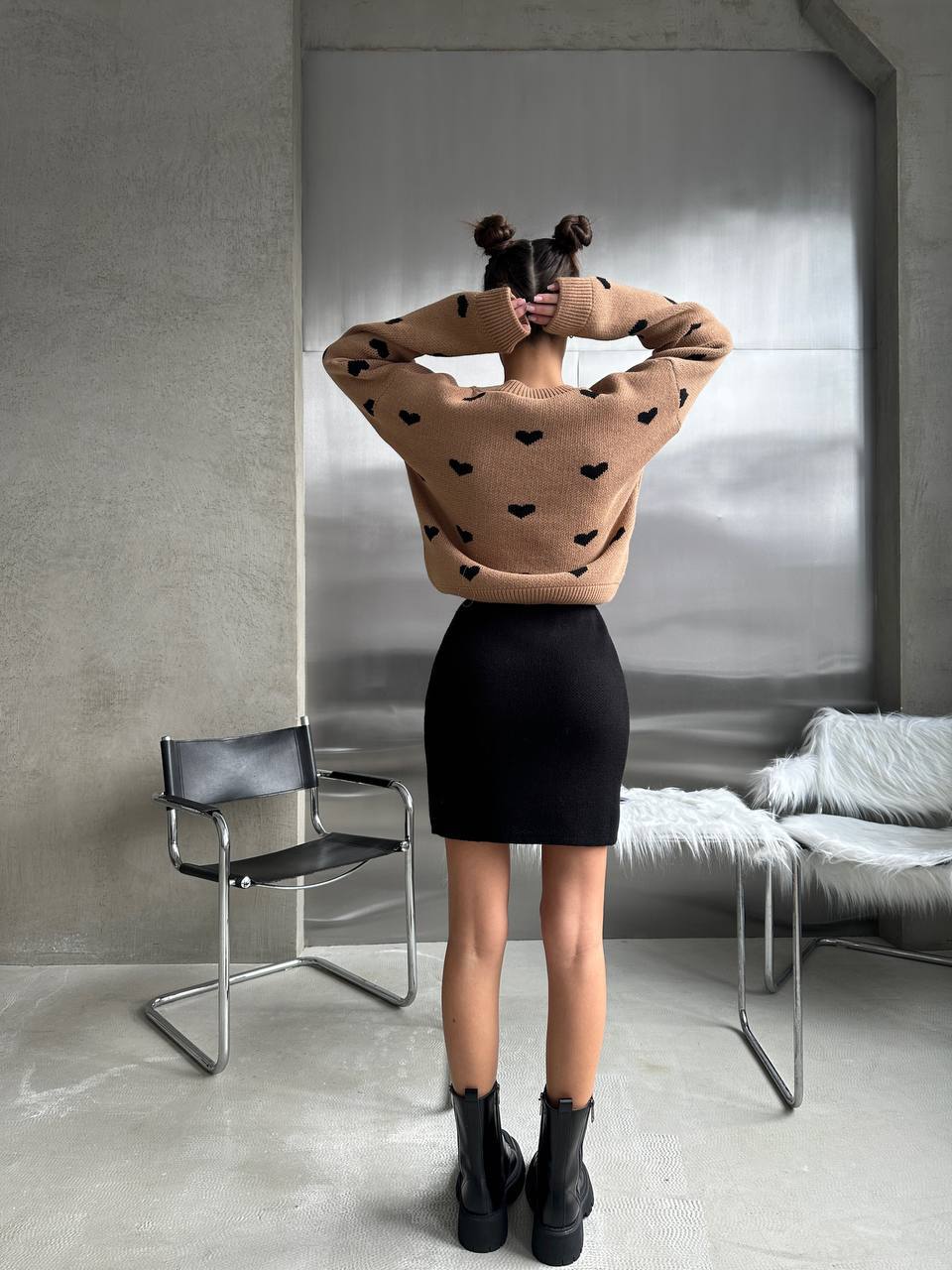 Person wearing a brown sweater with black heart patterns in a minimalistic room.