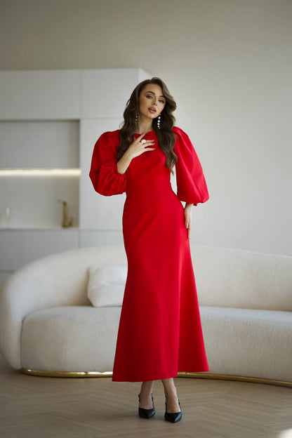 Woman in a red dress standing in a modern room with a white sofa and light-colored walls.