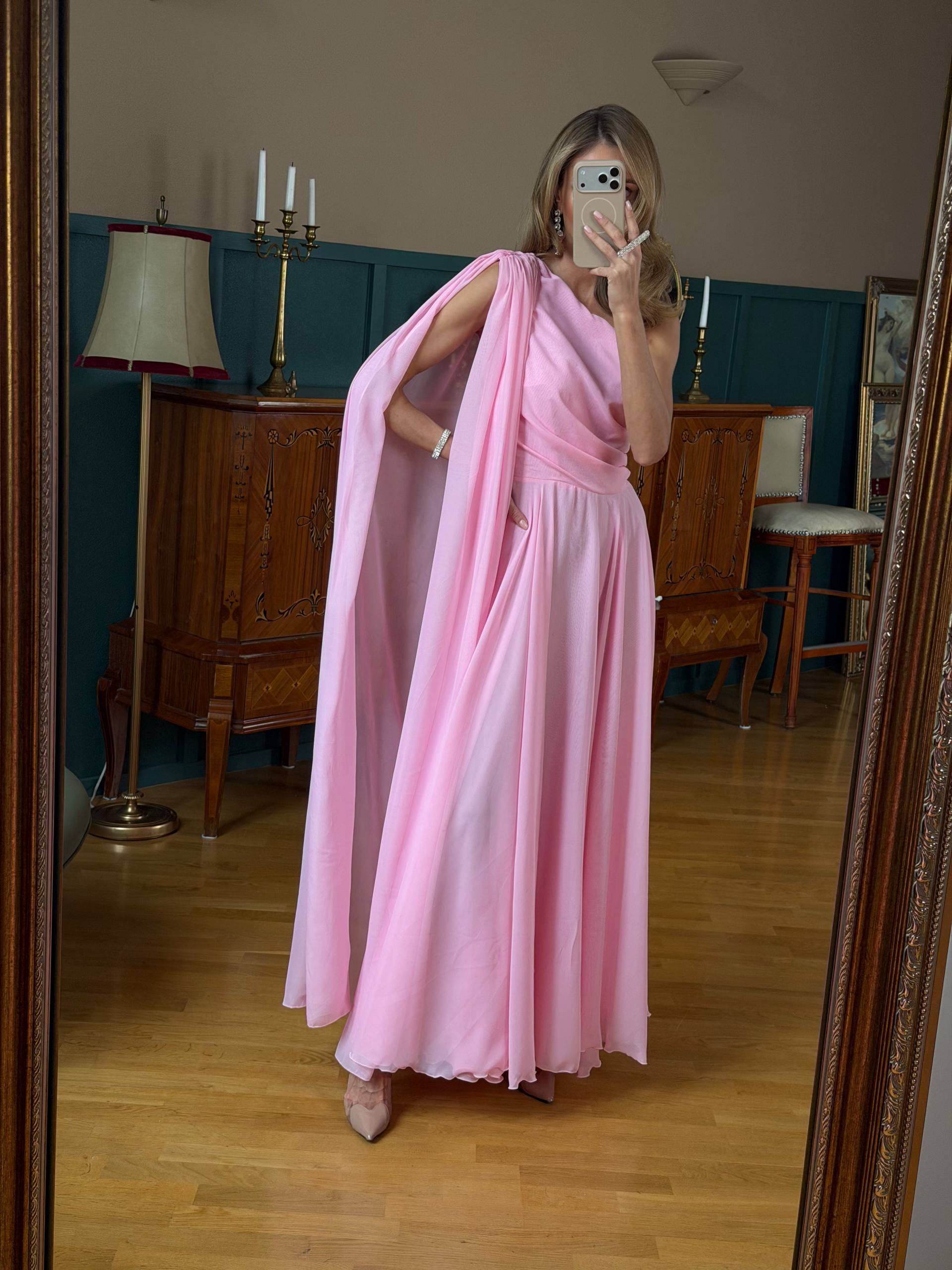 Woman in a pink dress taking a mirror selfie in a room with wooden furniture and a lamp.
