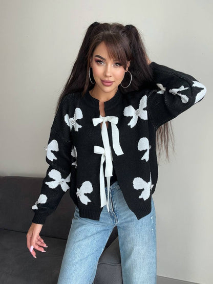 Woman wearing a black cardigan with white bow patterns and light blue jeans.