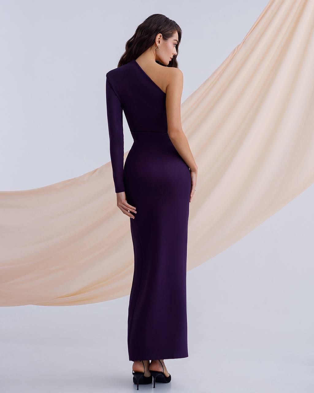 Woman wearing a one-shoulder purple evening gown with a beige fabric draped behind her.