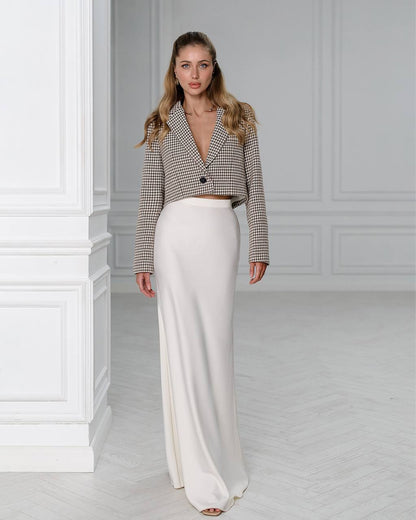 Woman wearing a checkered blazer and white pants in a minimalistic room.