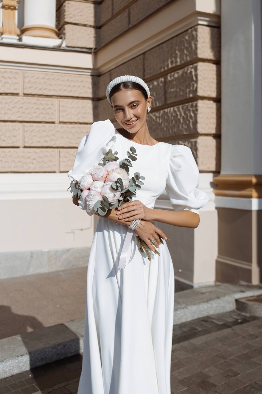 Woman in a white dress holding a bouquet of flowers in front of a building.