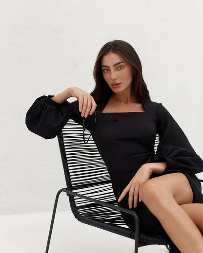 Woman in a black outfit sitting on a modern chair with a white background