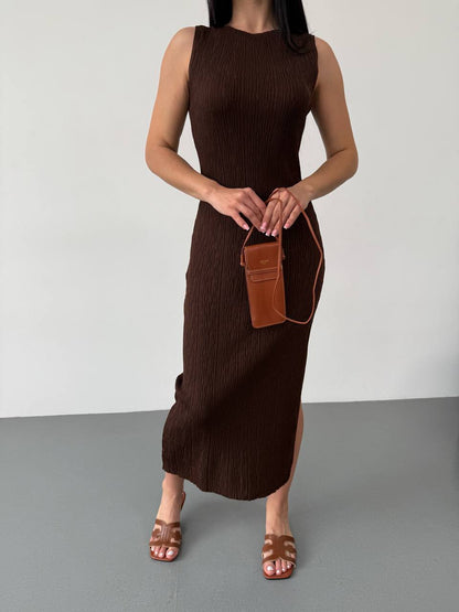 Woman wearing a brown sleeveless dress holding a matching brown handbag against a plain background