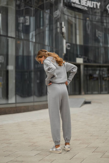 Person wearing a gray tracksuit standing on a sidewalk with a building in the background