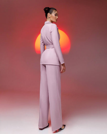 Woman in a pink suit standing against a gradient background with a sun-like design.