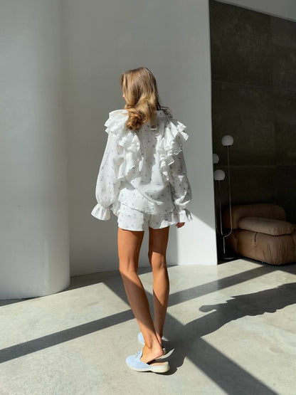 Woman wearing a white ruffled blouse and shorts in a modern room.