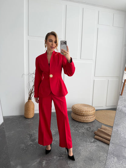 Person wearing a red suit taking a mirror selfie in a room with a white paneled wall and woven ottomans.