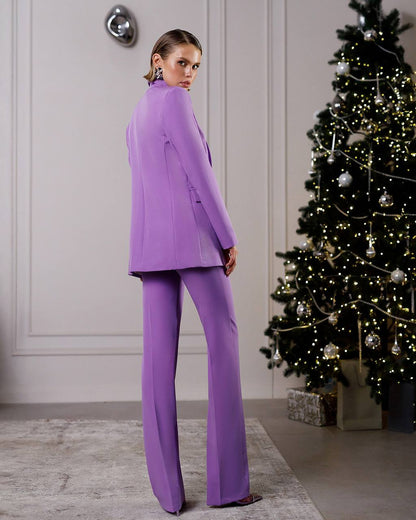 Woman in a purple suit standing in front of a decorated Christmas tree.