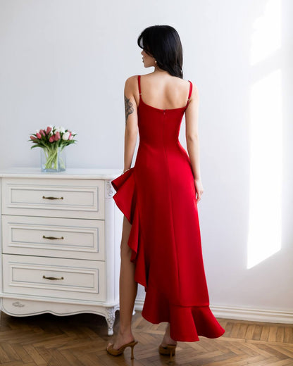 Woman in a red dress standing in a room with a white dresser and flowers.