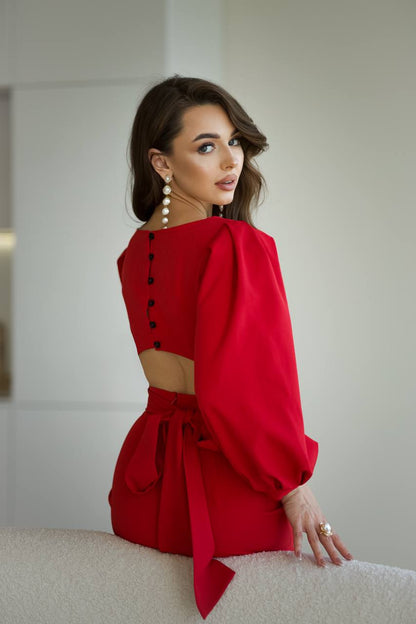 Woman wearing a red dress with a cut-out design, sitting on a white surface.