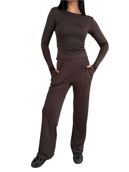 Person wearing a brown long-sleeve top and pants on a white background