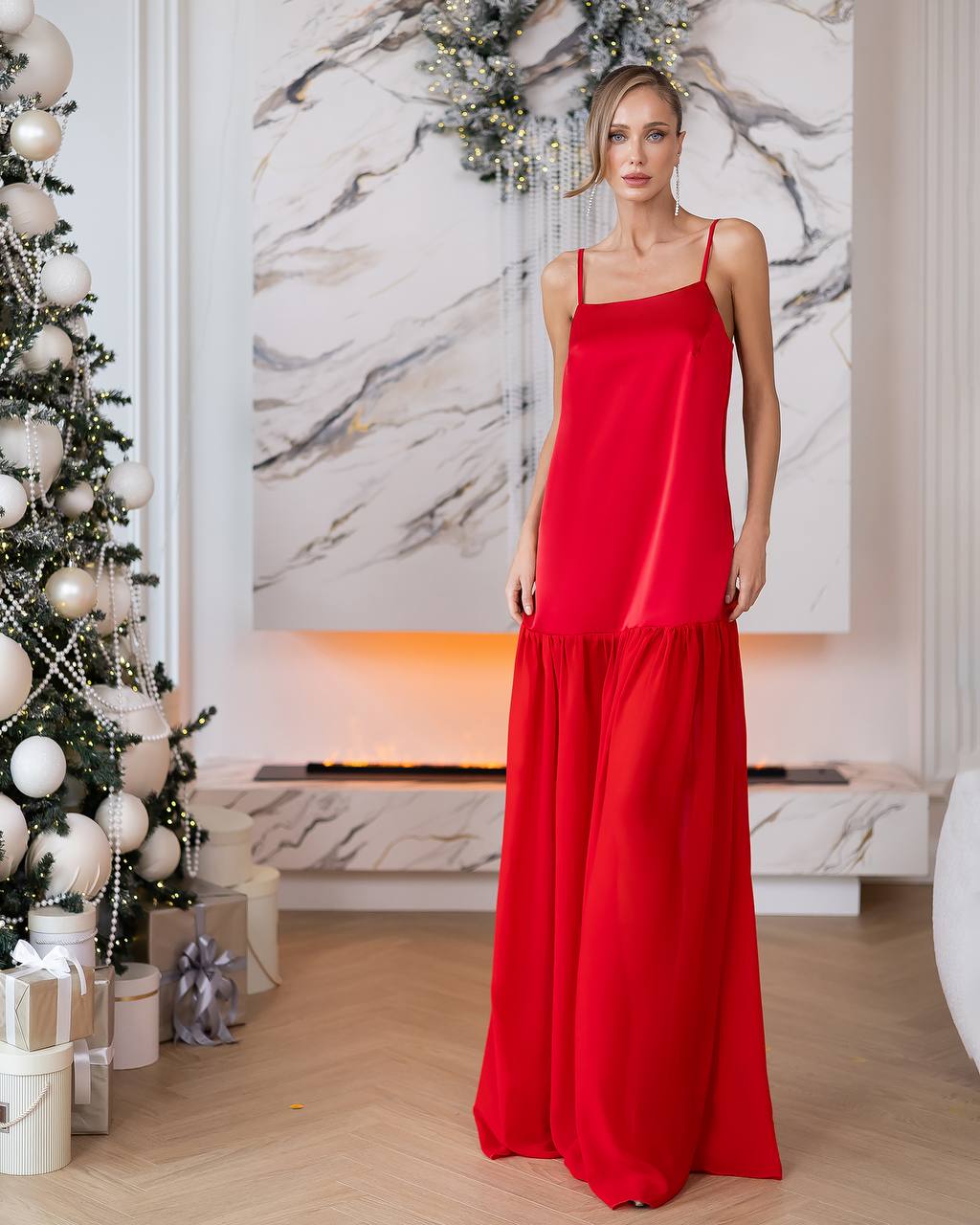 Woman in a red dress standing in a stylish room with a Christmas tree and marble wall.