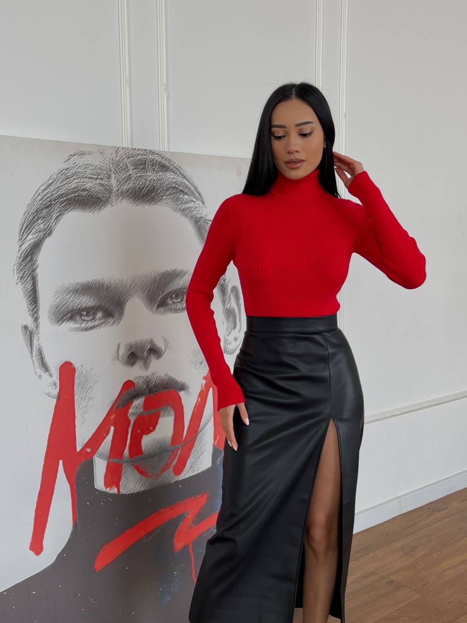 Woman in a red sweater and black skirt standing in front of a wall with a graphic design.