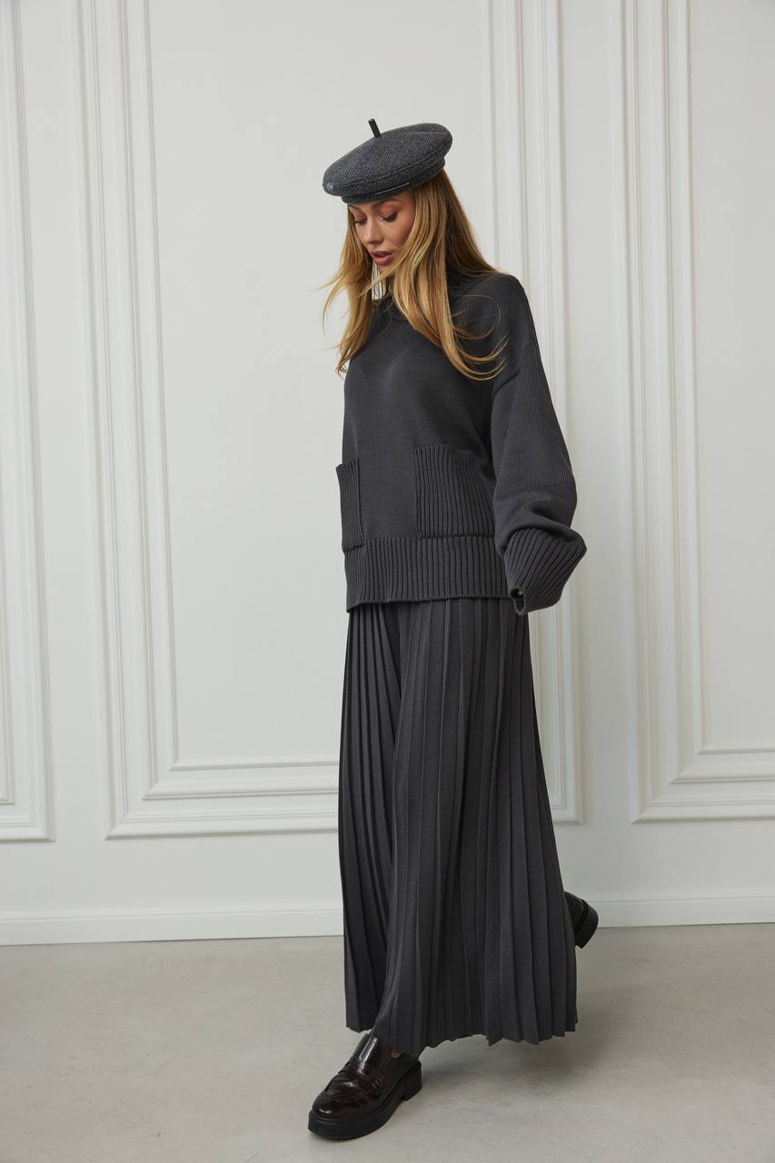 Person wearing a dark gray outfit with a beret against a white paneled wall.