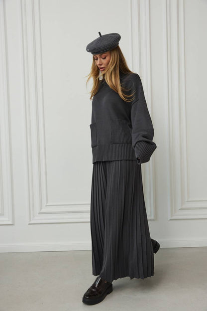 Person wearing a dark gray outfit with a beret against a white paneled wall.