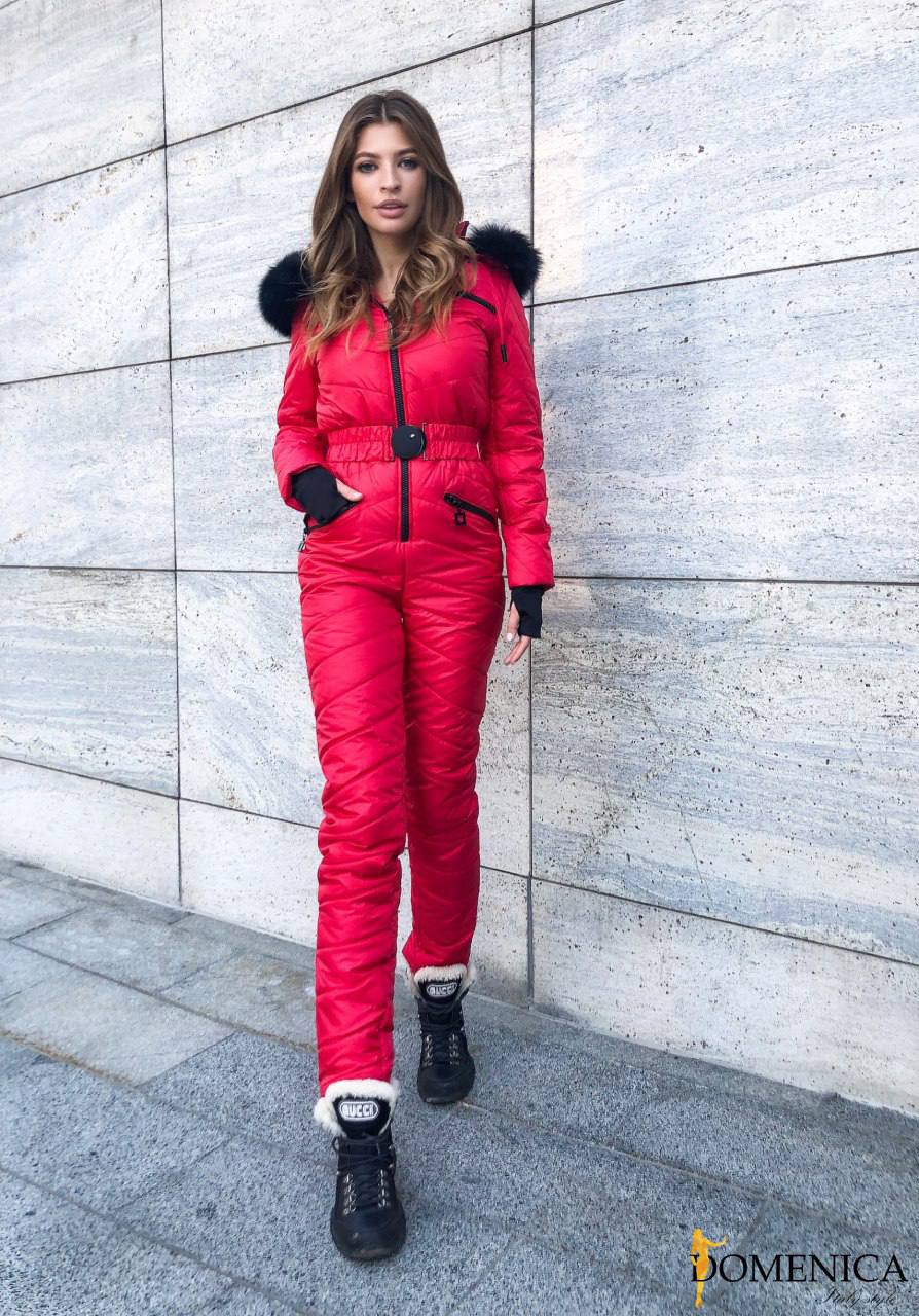 Woman wearing a red snowsuit with black fur trim against a gray concrete wall.