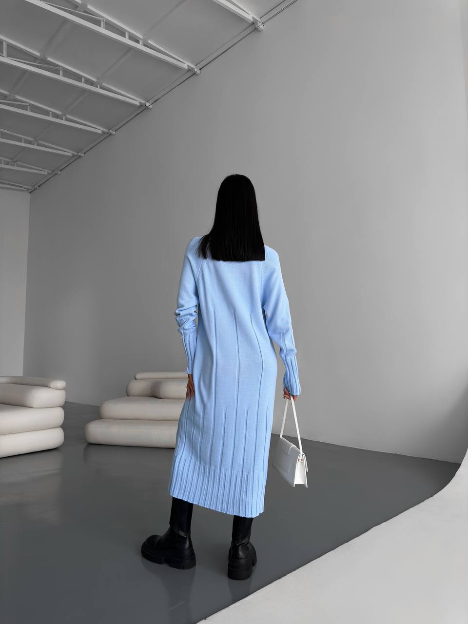 Person wearing a light blue dress in a minimalistic room with gray walls and white ceiling.