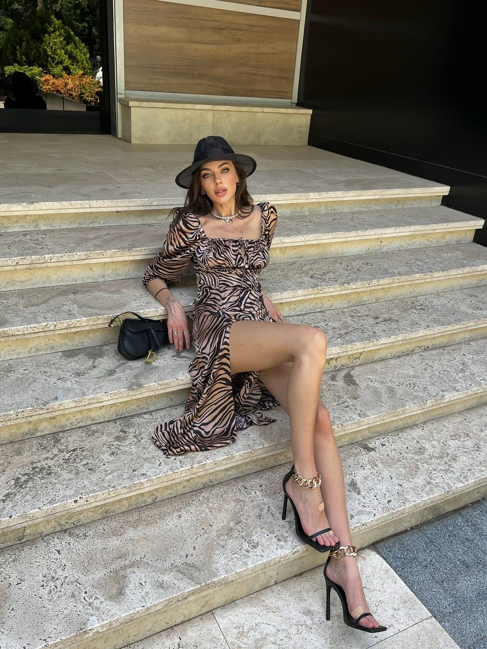 Woman in a patterned dress and black hat sitting on stone steps.