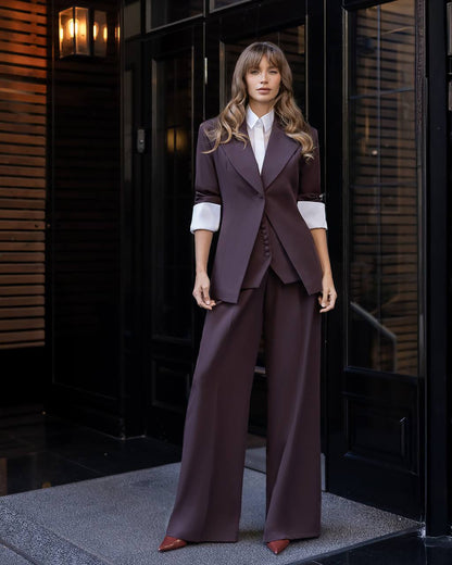 Woman in a brown suit standing in front of a dark door.