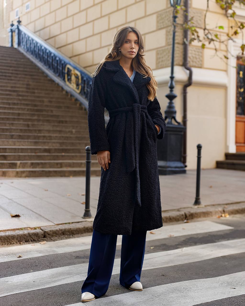 Woman in a long black coat standing on a city street.