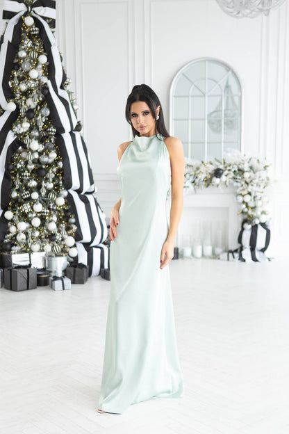 Woman in a light green dress standing in a decorated room with Christmas trees and gifts.