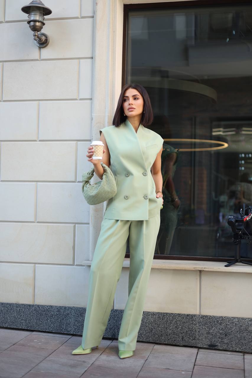 Woman in a light green outfit holding a coffee cup, standing outside a building.