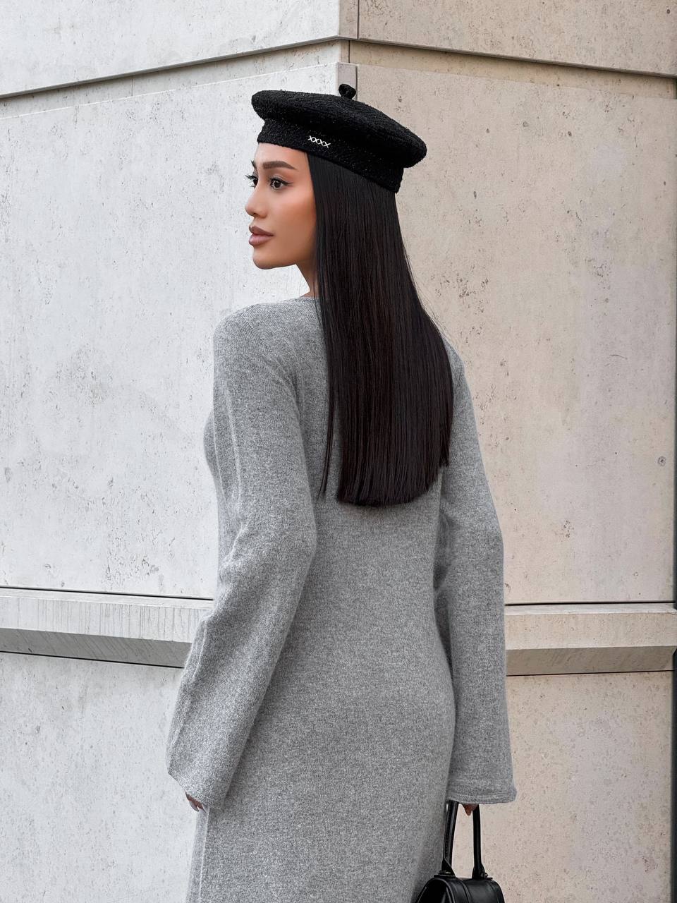 Woman wearing a black beret and gray dress against a light stone wall.