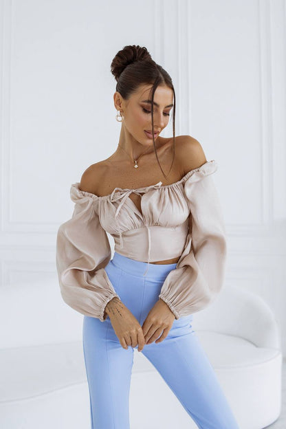 Woman wearing a beige off-shoulder top and light blue pants against a white background