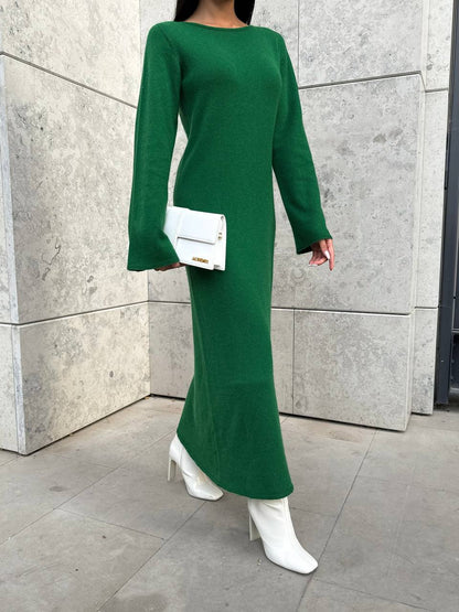 Person wearing a green dress with white boots and a white clutch against a gray wall.