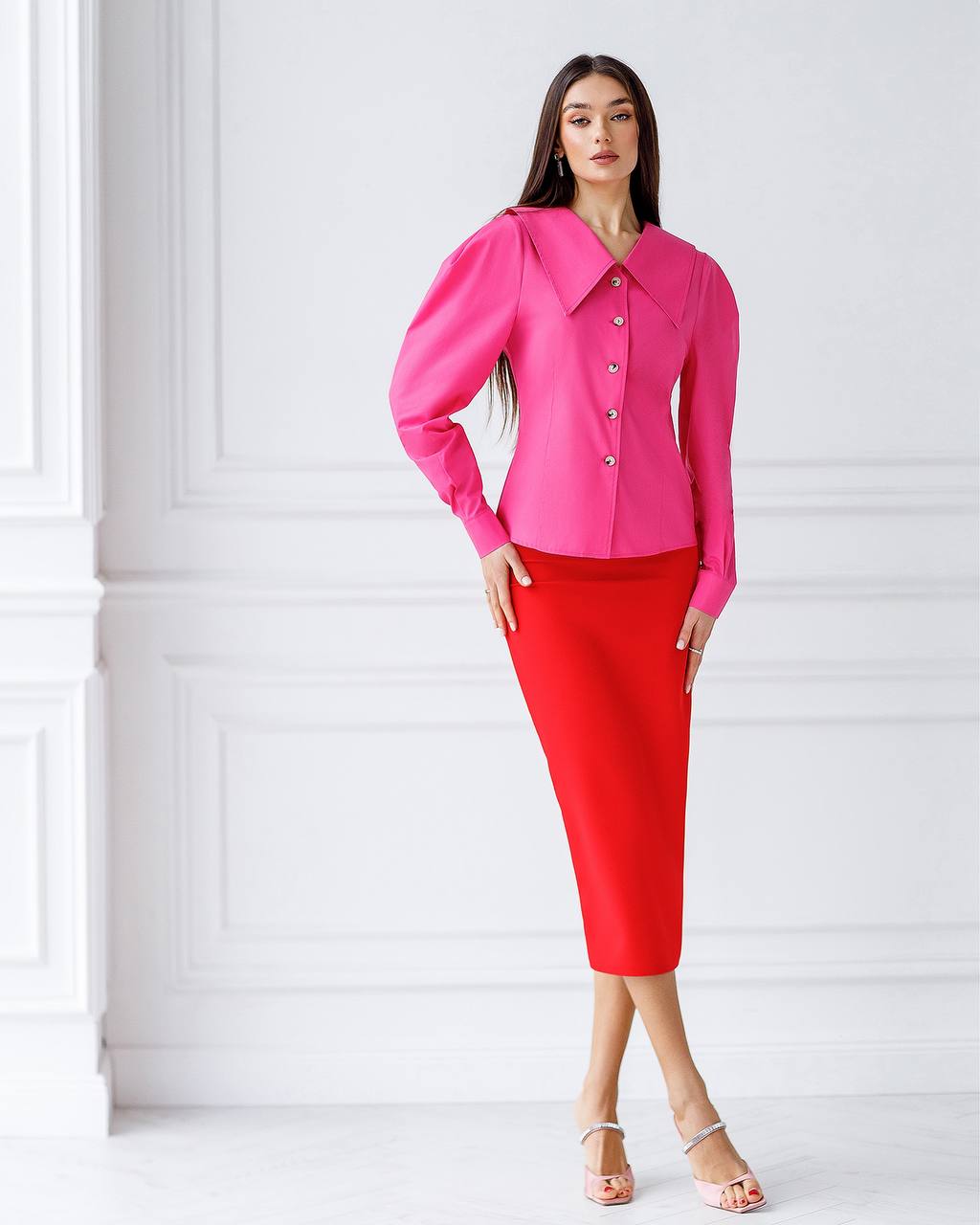 Woman wearing a bright pink blouse and red skirt against a white background