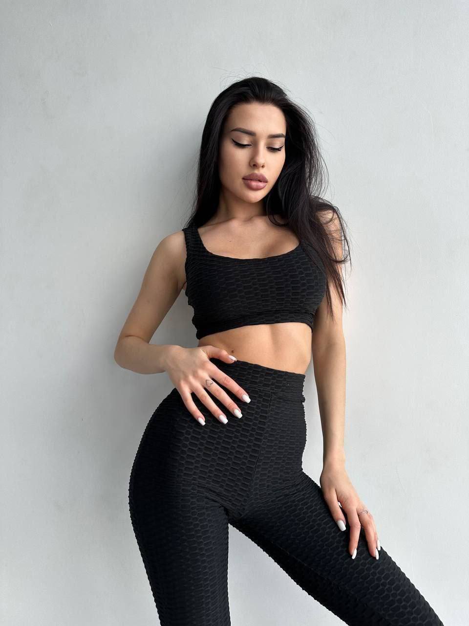 Woman wearing a black textured sports bra and leggings against a gray background