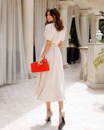 Woman in a white dress holding a red clutch in an elegant outdoor setting.