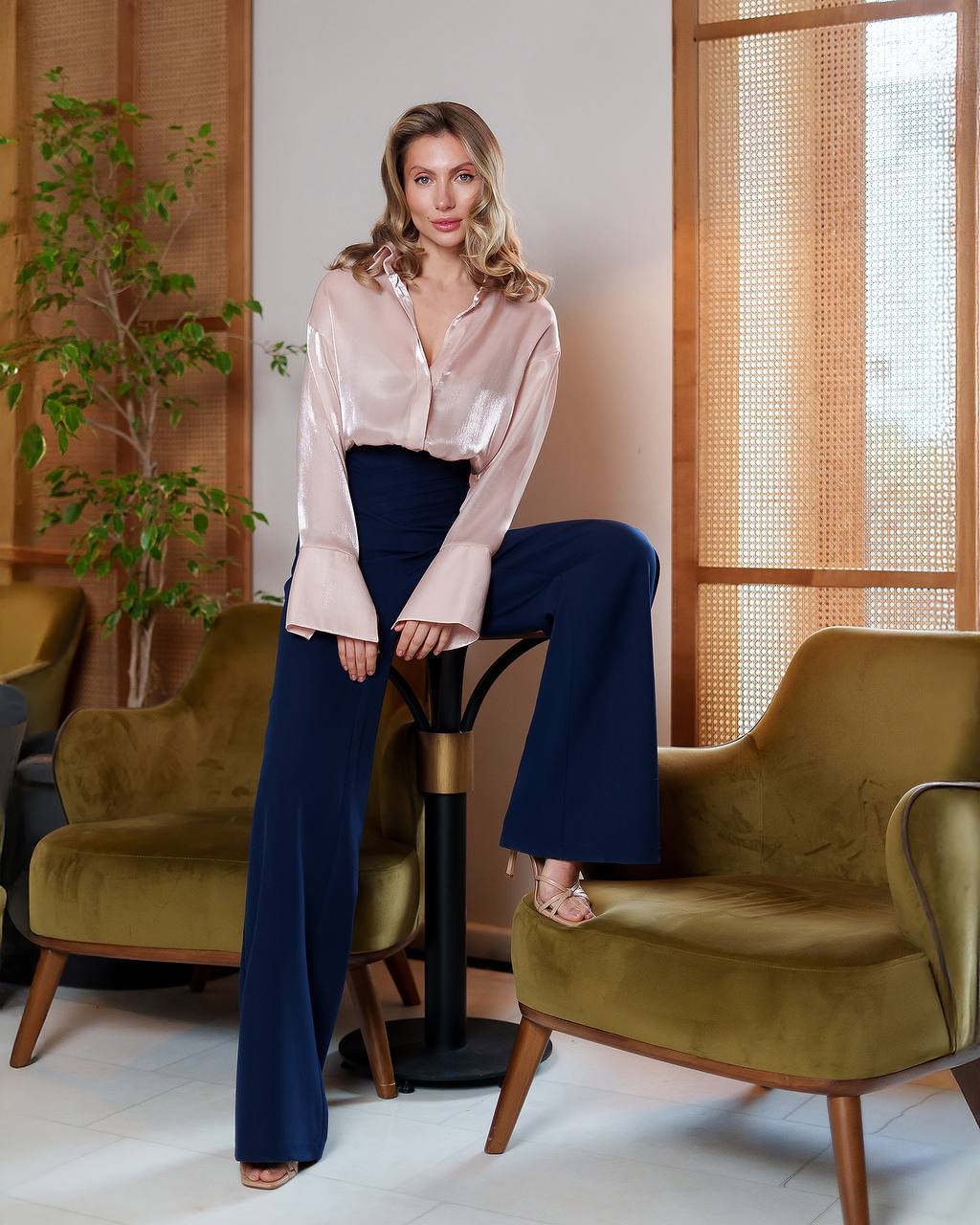Woman sitting on a chair in a stylish room with plants and furniture.