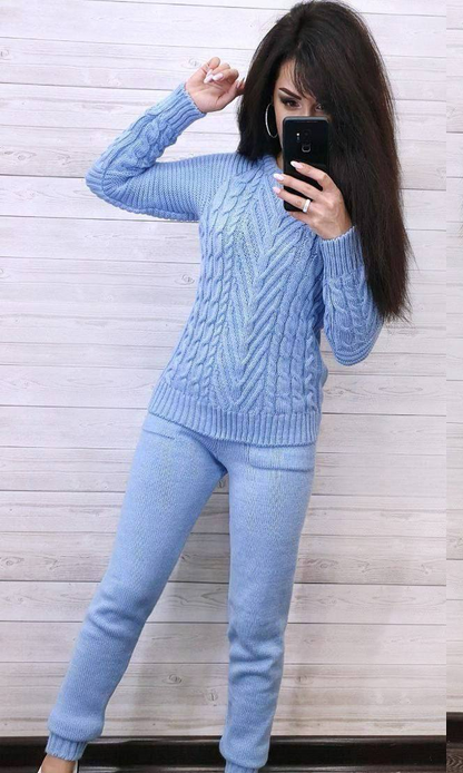 Woman wearing a light blue cable knit sweater and pants against a wooden background