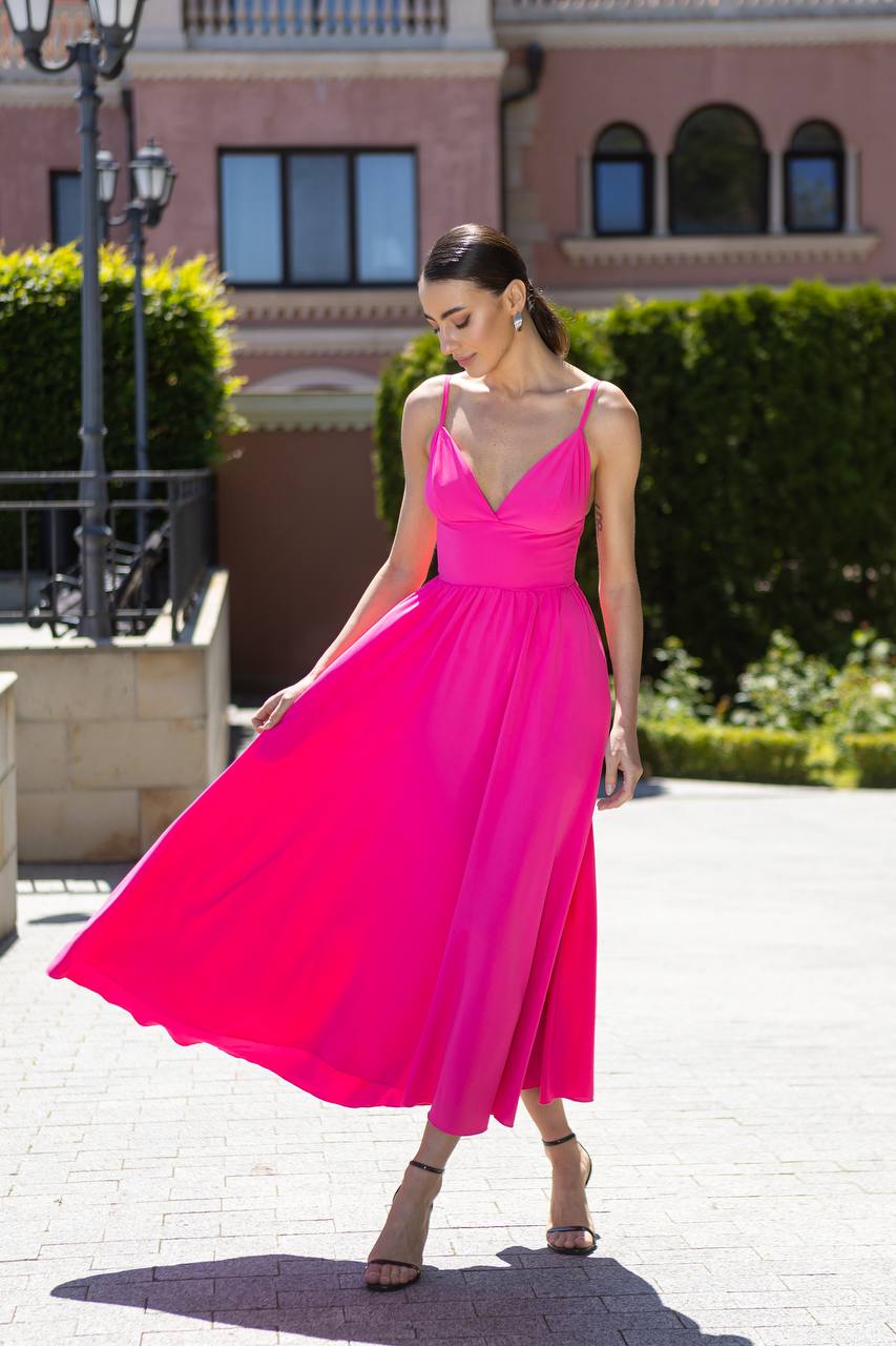 Woman in a bright pink dress standing outdoors with a building and greenery in the background