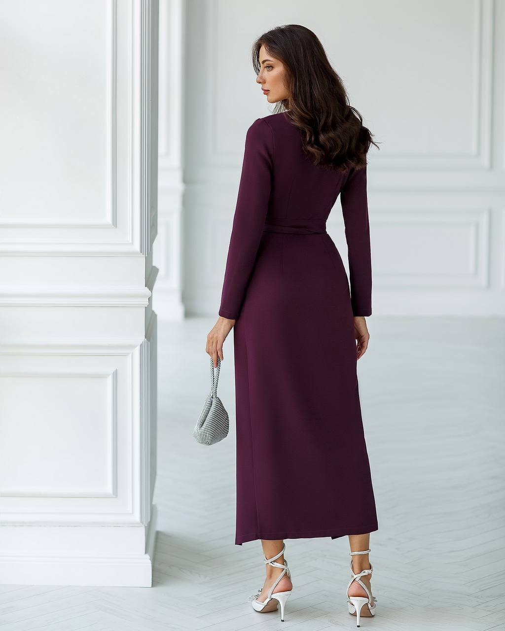 Woman wearing a long burgundy dress against a white wall