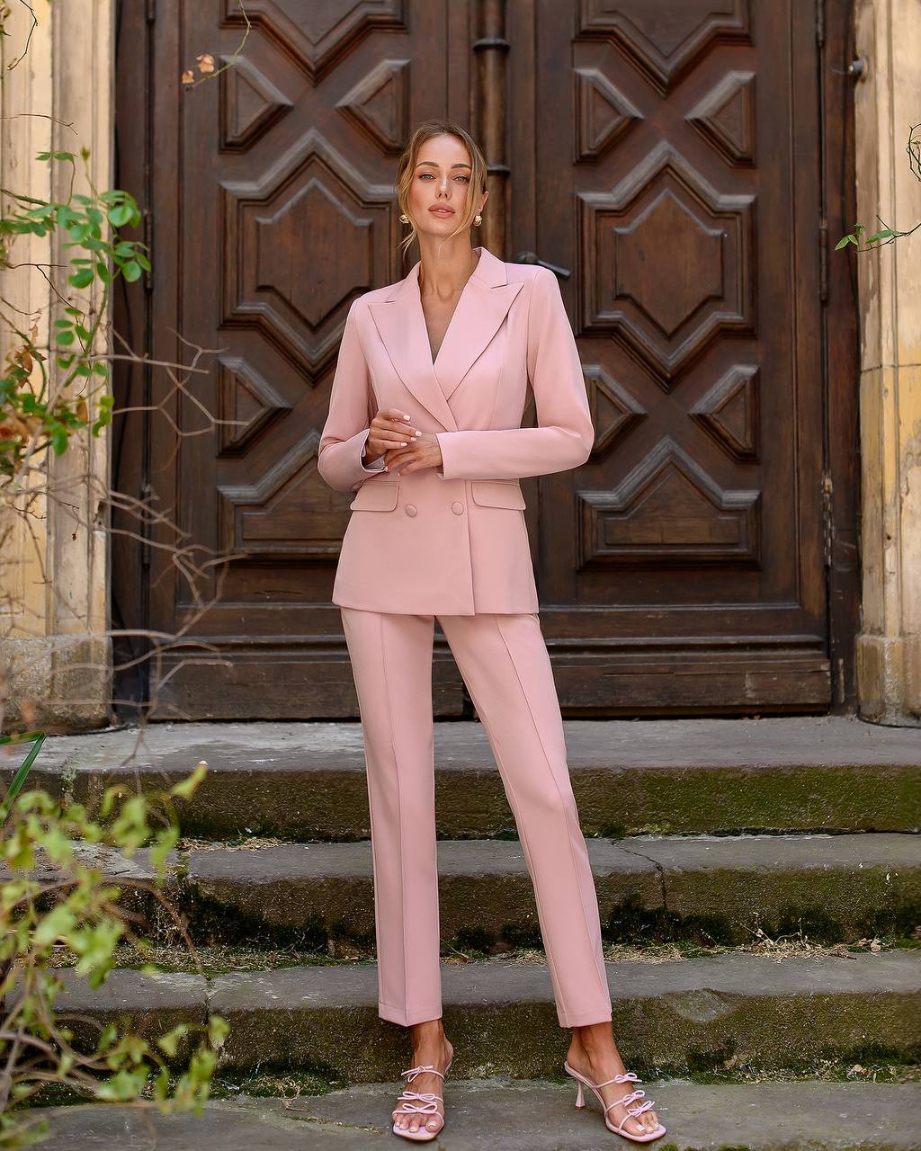 Woman in a pink suit standing in front of a wooden door.