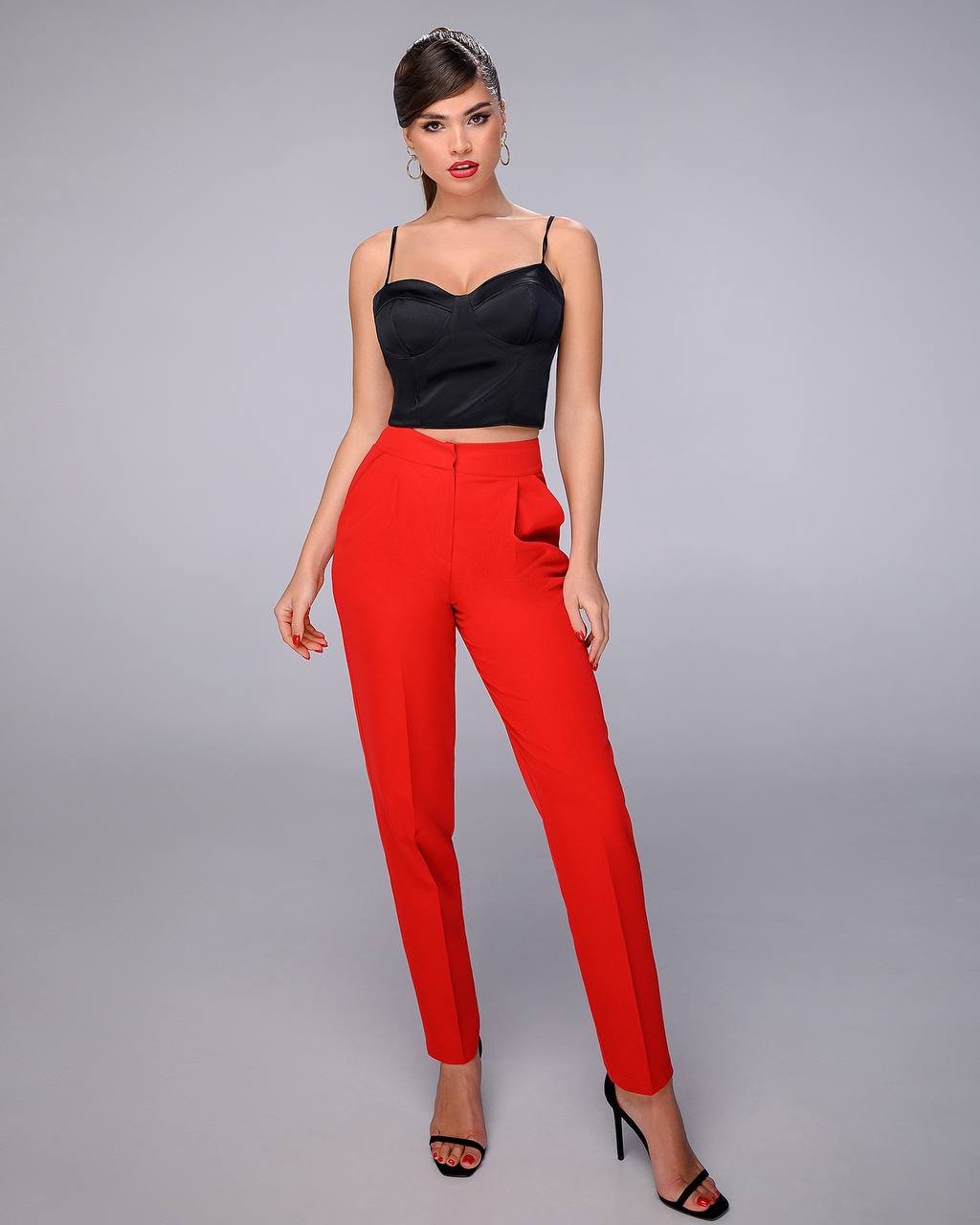 Woman wearing a black top and red pants on a gray background