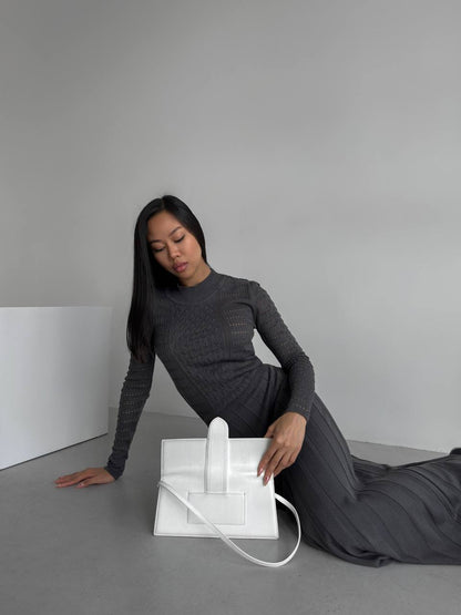 Woman in a gray dress sitting on the floor with a white electronic device.