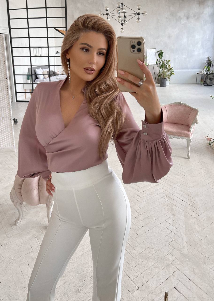 Woman taking a mirror selfie wearing a mauve top and white pants in a stylish room.