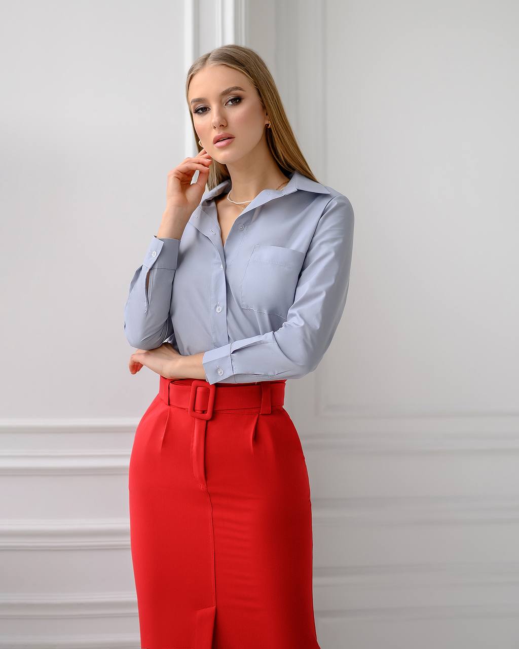 Woman wearing a light blue shirt and red pants against a white wall