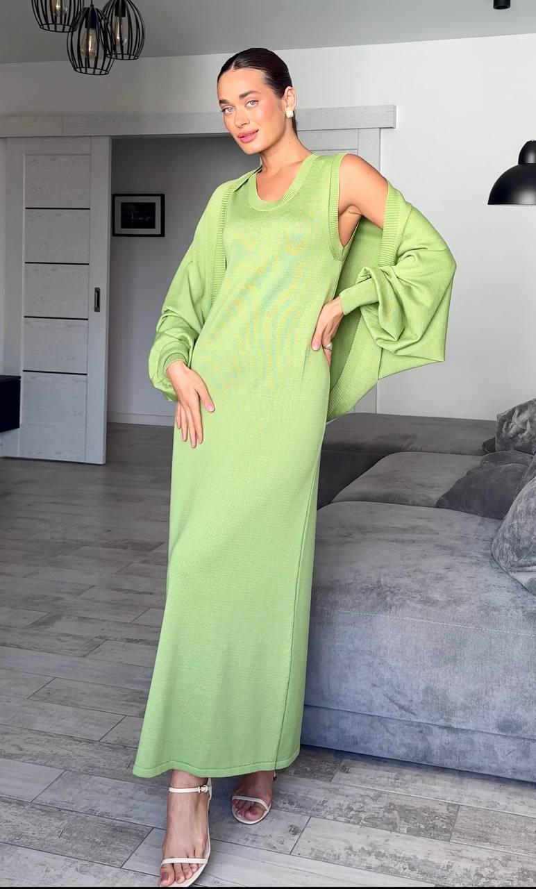 Woman in a green dress standing in a living room with a gray sofa and white walls.