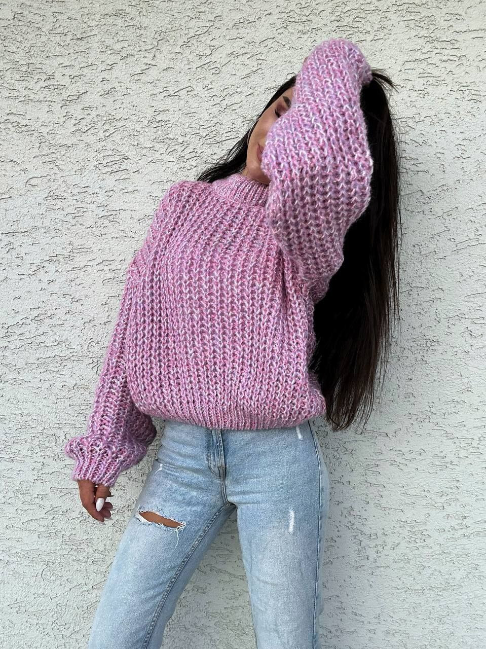 Person wearing a pink chunky knit sweater and light blue jeans against a textured wall.