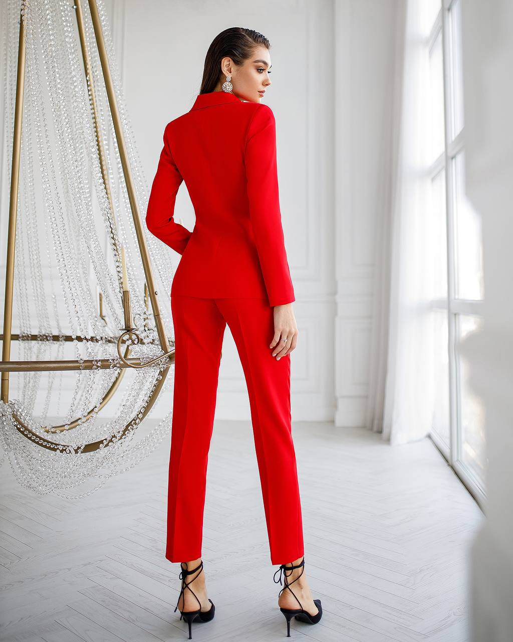 Woman wearing a red suit standing in a bright room with large windows.