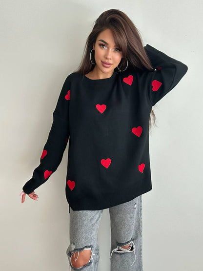 Woman wearing a black sweater with red heart patterns against a plain background
