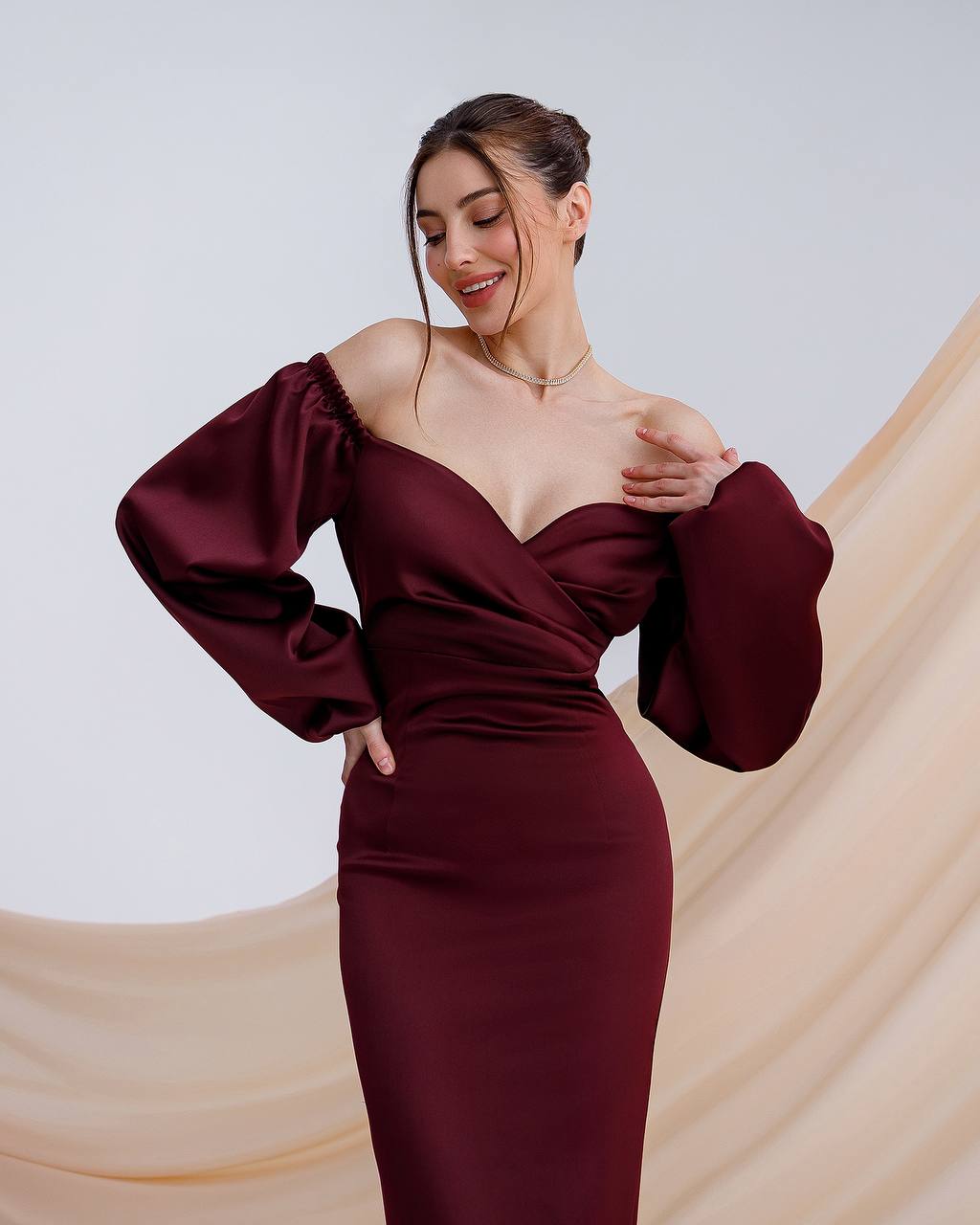 Woman wearing a burgundy off-shoulder dress with long sleeves against a beige and white background